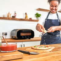 Ooni Volt 12 Electric pizza oven. person grating cheese in front of oven 